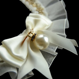 May include: A white satin bow with a pearl and rhinestone embellishment, attached to a white tulle collar.