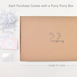 May include: A brown cardboard box with the text "furryfurry" printed on it. The box is 25 inches tall and 41 inches wide. The box is surrounded by white tissue paper, a pink and blue card with the text "furryfurry" printed on it, and a sticker with the same text. The text "Each Purchase Comes with a Purry Purry Box" is printed above the box.