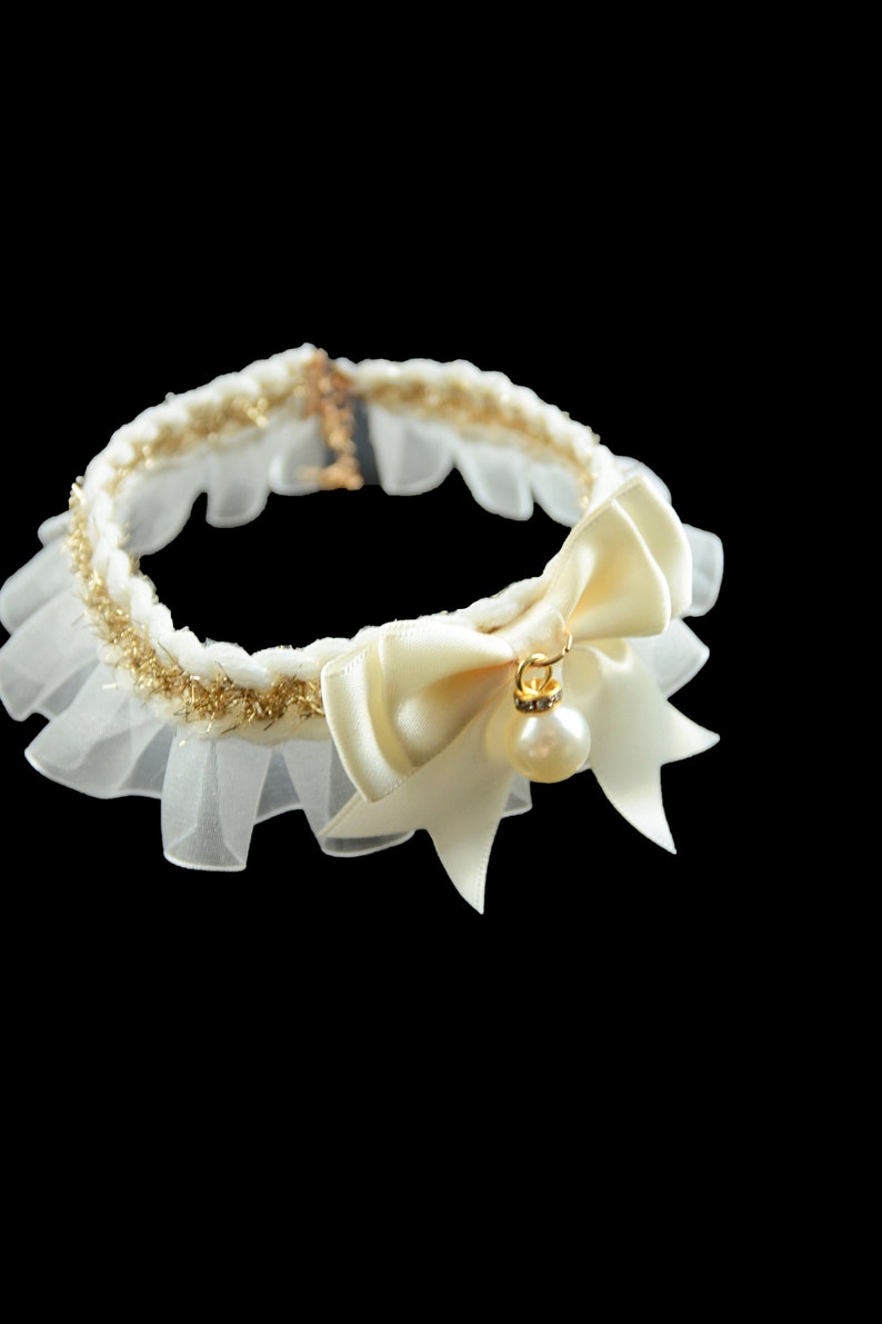 May include: A white lace choker with a gold trim and a large ivory satin bow with a pearl and rhinestone pendant.