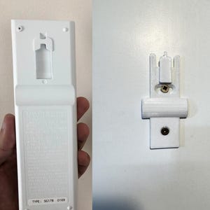 Może przedstawiać: Biały pilot i pasujący uchwyt ścienny. Na pilocie znajduje się napis "TYPE: SG17B 0169". Uchwyt ścienny został zaprojektowany tak, aby bezpiecznie trzymać pilota. Pilot i uchwyt ścienny są wykonane z tworzywa sztucznego.