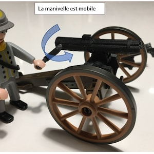 Puede incluir: Un soldado de juguete con uniforme gris y sombrero amarillo est&aacute; girando la manivela de un ca&ntilde;&oacute;n de juguete negro sobre ruedas. El ca&ntilde;&oacute;n tiene una rueda de madera marr&oacute;n y un marco de metal gris. El texto "La manivelle est mobile" est&aacute; escrito en blanco sobre un rect&aacute;ngulo negro encima del ca&ntilde;&oacute;n.
