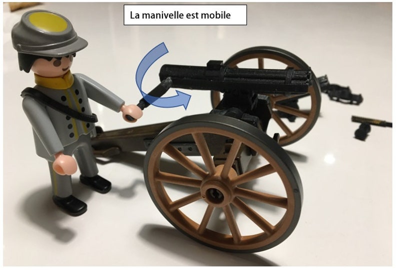 Puede incluir: Un soldado de juguete con uniforme gris y sombrero amarillo est&aacute; girando la manivela de un ca&ntilde;&oacute;n de juguete negro sobre ruedas. El ca&ntilde;&oacute;n tiene una rueda de madera marr&oacute;n y un marco de metal gris. El texto "La manivelle est mobile" est&aacute; escrito en blanco sobre un rect&aacute;ngulo negro encima del ca&ntilde;&oacute;n.