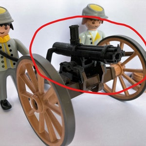 Puede incluir: Un juguete de ca&ntilde;&oacute;n Gatling negro montado en un carro de madera con dos ruedas marrones. El ca&ntilde;&oacute;n tiene un ca&ntilde;&oacute;n de metal y un mango de madera. El carro est&aacute; hecho de madera y tiene un eje de metal.