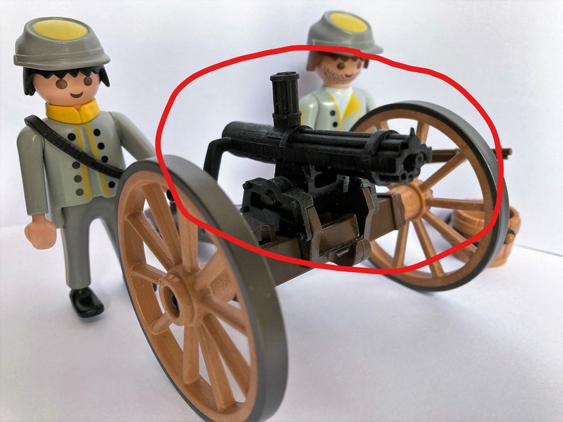 Puede incluir: Un juguete de ca&ntilde;&oacute;n Gatling negro montado en un carro de madera con dos ruedas marrones. El ca&ntilde;&oacute;n tiene un ca&ntilde;&oacute;n de metal y un mango de madera. El carro est&aacute; hecho de madera y tiene un eje de metal.