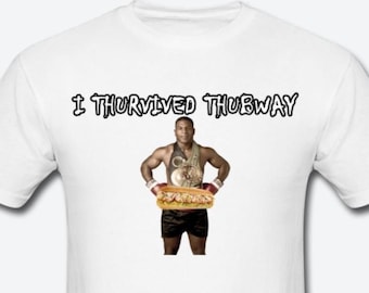Puede incluir: Camiseta blanca con el texto "I THURSIVED THUBWAY" impreso en negro. Una foto de un boxeador sosteniendo un gran sándwich está impresa en la camiseta.