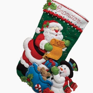 Könnte beinhalten: Ein Weihnachtsstrumpf mit grünem Hintergrund, der den Weihnachtsmann, einen Schneemann und den Namen "Brandon" zeigt. Der Strumpf ist mit Stechpalmen, Pailletten und verschiedenen Geschenken verziert.