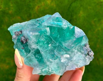 Könnte beinhalten: Ein großer, grüner Fluoritkristall mit einem hellblauen Farbton. Der Kristall hat eine raue, natürliche Textur und besteht aus vielen kleineren Kristallen.
