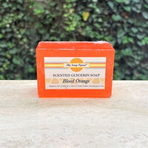 Pu&ograve; includere: Una saponetta rettangolare di glicerina profumata all'arancia con il testo "The Soap Opera&reg;" e "SCENTED GLYCERIN SOAP Blood Orange" sull'etichetta. L'etichetta include anche il testo "Madison, WI | (608) 251-4051 | Order Online: thesoapopera.com".