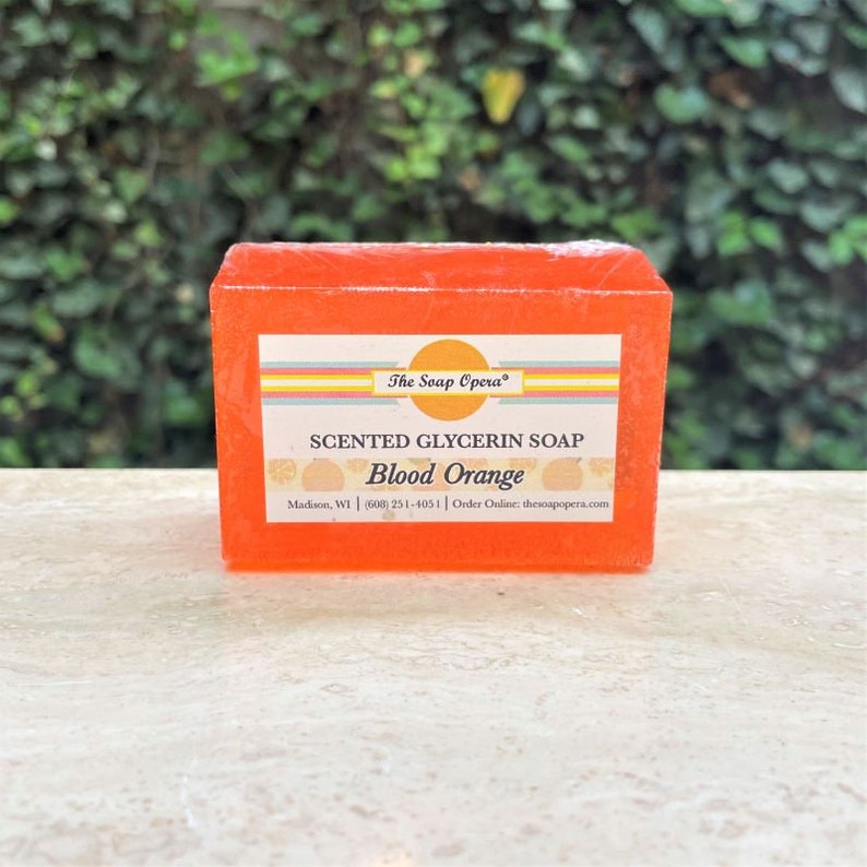 Pu&ograve; includere: Una saponetta rettangolare di glicerina profumata all'arancia con il testo "The Soap Opera&reg;" e "SCENTED GLYCERIN SOAP Blood Orange" sull'etichetta. L'etichetta include anche il testo "Madison, WI | (608) 251-4051 | Order Online: thesoapopera.com".