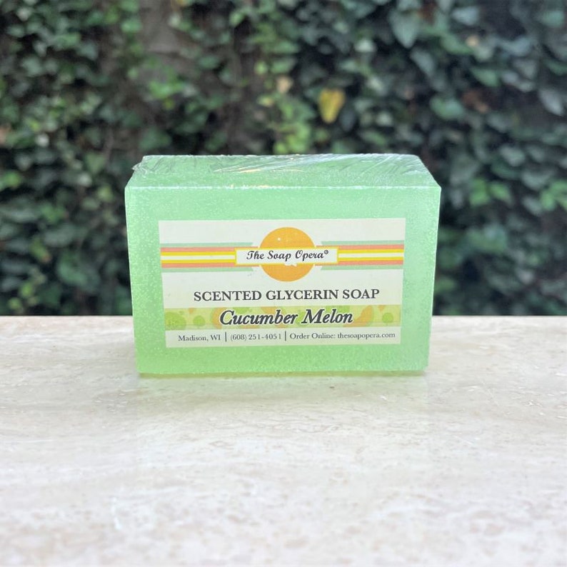 Pu&ograve; includere: Una saponetta di glicerina verde con un'etichetta bianca su cui &egrave; scritto "The Soap Opera" in lettere arancioni. L'etichetta riporta anche la scritta "Sapone alla glicerina profumato Melone e Cetriolo" e contiene le informazioni di contatto dell'azienda.