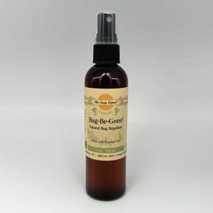 May include: A brown glass bottle with a black spray top. The label is beige with green and yellow accents. The label reads "The Soap Opera naturals Bug-Be-Gone! Natural Bug Repellent Made with Essential Oils 4 oz 118 ml".