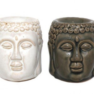 May include: Two ceramic Buddha head incense burners, one white and one dark green. Both have closed eyes and a serene expression.