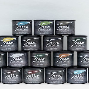 May include: A pyramid display of 16 small paint cans, each with a black lid and a label that reads "Terra Clay Paint" and a different color name. The colors include: Genelean Blue, Pistachio, Desert Tan, Daffodil, Galaxy, Blue Moon, Malachite, Onyx, Moon Beam, Blue Agave, Marigold, Wisteria Mist, Wheat, Blackberry, Bougainvillea, London Blue,  Lant's Lagoon, and Prairie Dawn.