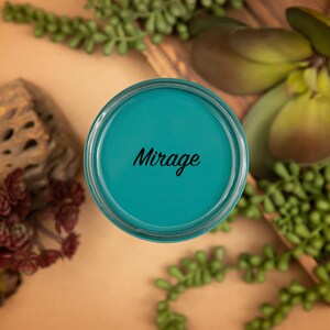 May include: A teal blue paint sample jar with the word "Mirage" printed in black on the label.