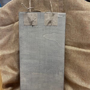 K&ouml;nnte beinhalten: Eine graue Papiert&uuml;te mit zwei braunen Papierquadraten, die auf die Vorderseite geklebt sind. Die Tasche hat einen Seilgriff.