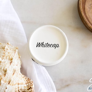 May include: A white paint sample jar with the text "Whitecap" on the label. The jar is sitting on a white surface.