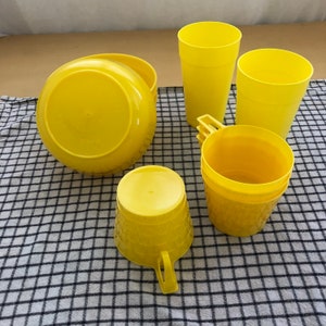 May include: A set of yellow plastic cups and bowls. The cups are stacked and have a textured design. The bowls are plain and round.