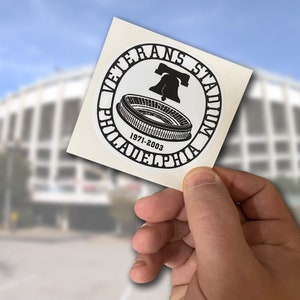 May include: A black and white sticker with the text "Veterans Stadium Philadelphia 1971-2003" and a graphic of the Liberty Bell and a stadium.
