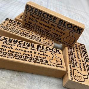 May include: Three wooden blocks with the text "Exercise Block" and instructions to "Place block on floor, Walk around it twice, Sit down and relax! Congratulations! You have just walked around the block twice!" printed on them. Each block has a thumbs up icon.