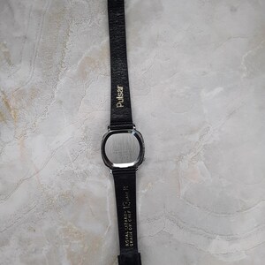 May include: A vintage Pulsar watch with a rectangular silver-tone case and a black leather band. The band is marked with "Pulsar" and "Royal Lizard - 13, AM R Grain on Calf". The watch has a silver buckle.