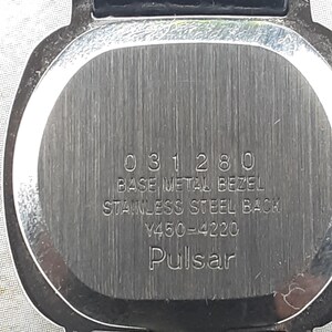 May include: Close-up of a watch back with a silver-colored, brushed metal finish. The watch has a black leather band. The text on the watch reads "031280 BASE METAL BEZEL STAINLESS STEEL BACK Y450-4220 Pulsar."