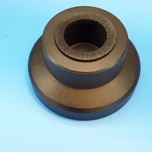 May include: A black, cylindrical object with a flared base and a central opening lined with a dark, textured material. The object is set against a light blue background, showcasing its shape and design.