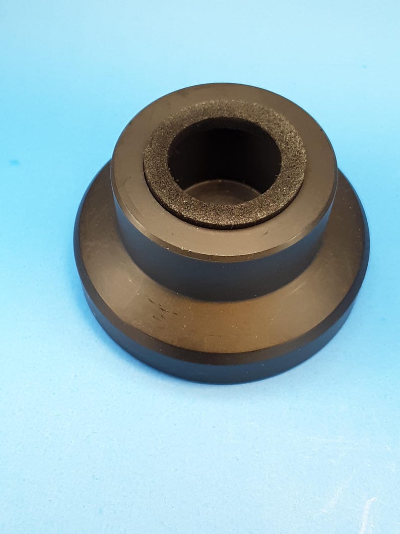 May include: A black, cylindrical object with a flared base and a central opening lined with a dark, textured material. The object is set against a light blue background, showcasing its shape and design.