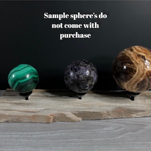 May include: Three polished gemstone spheres on a wooden stand. The spheres are green, purple, and brown with swirling patterns. The text "Sample sphere's do not come with purchase" is visible above the spheres.