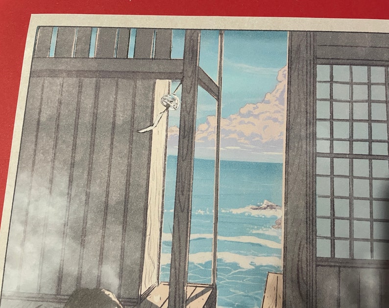 May include: A woodblock print depicting a view of the ocean from a Japanese home. The print features a wooden window frame with a view of the ocean and sky. The ocean is a light blue colour with white waves. The sky is a light blue colour with white clouds. The print is framed in a wooden frame.