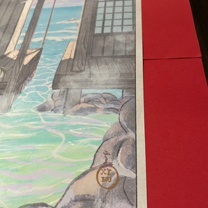 May include: A Japanese woodblock print showing a view of a wooden structure with a window overlooking a body of water. The water is a light blue and green colour and there are rocks in the water. The print is signed with a red seal in the bottom right corner.