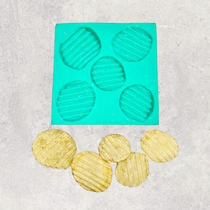 May include: A turquoise silicone mold with six round cavities, each with a ridged pattern.  There are six golden brown potato chips next to the mold.