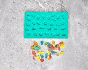 May include: A turquoise silicone mold with multiple small, irregular shapes. The mold is filled with colorful candy pieces.