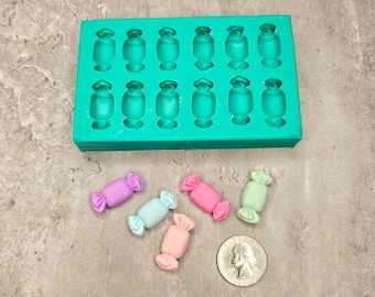 May include: A green silicone mold with 16 candy-shaped cavities. Five small candy-shaped pieces are shown in various pastel colors: light blue, pink, light green, and purple.