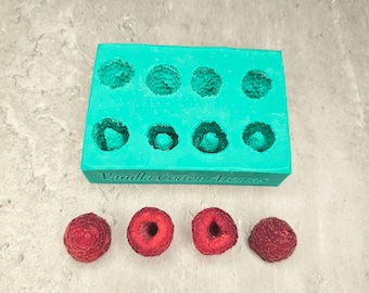 May include: A teal silicone mold with nine round cavities, labeled "Vanilla Cotton Aromas". Four red raspberries are shown below the mold.