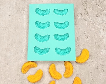 May include: A turquoise silicone mold with eight cavities shaped like orange slices.  There are eight orange slices on a gray surface next to the mold.