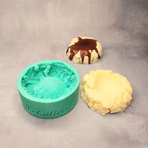 May include: A teal silicone mold with the text "Vanilla Cotton" on the side. Two finished products are shown, one with a chocolate topping and one without.