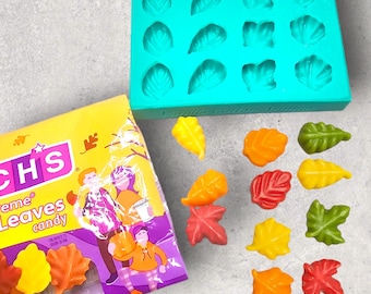 May include: A blue silicone mold with 12 leaf-shaped cavities.  The mold is filled with colorful candy leaves in various shades of red, orange, yellow, and green. The candy is arranged on a white surface. The candy is packaged in a bag with the text "Extreme Leaves Candy" printed on it.