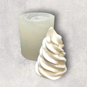 May include: A white, swirled soft-serve ice cream cone beside a clear silicone mould. The mould is cylindrical with the word "OMAS" faintly visible. The ice cream cone is a solid, smooth form, suggesting a craft or baking project.