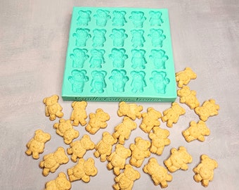 May include: A teal silicone mold with 36 bear-shaped cavities.  The mold is labeled "Vanilla Cotton Aromas".  There are 30 small, golden brown bear-shaped cookies scattered around the mold.