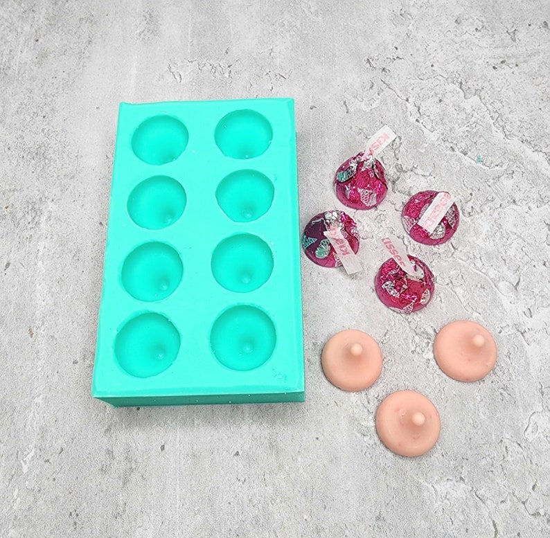 May include: A teal silicone mold with eight round cavities, perfect for making small candies or chocolates.  Five pink and silver foil-wrapped chocolates are scattered around the mold, along with three small, round, pink silicone molds.