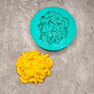 Könnte beinhalten: Eine grüne Silikonform in Form eines Maccaroni-Käse-Haufens. Neben der Form liegt ein gelber Maccaroni-Käse-Haufen.