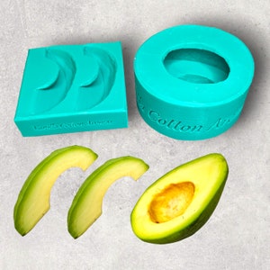 Puede incluir: Un juego de moldes de color turquesa para hacer artículos con forma de aguacate, con el texto "Vanilla Cotton Aromas" en un molde. También se muestran aguacates en rodajas. Los moldes están diseñados para crear jabones o velas con forma de aguacate.