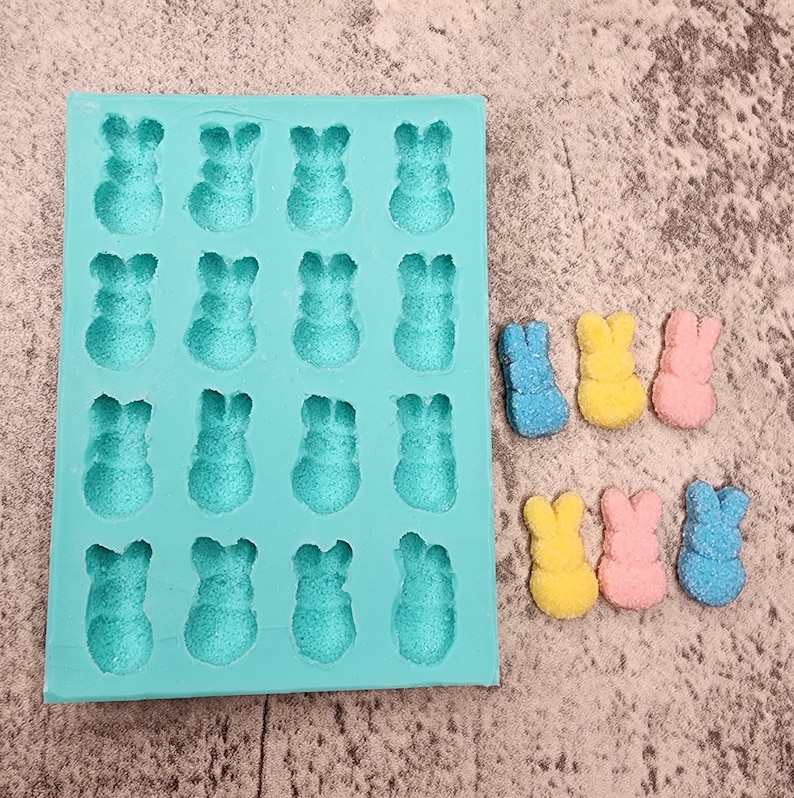May include: A teal silicone mold with 16 bunny-shaped cavities.  The mold is filled with colorful candy shaped like bunnies.  The candy is blue, yellow, and pink.