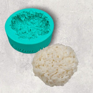 May include: A teal silicone mold shaped like a mound of rice. The mold has the words "Cotton Alley" printed on the bottom. A mound of white cooked rice is next to the mold.