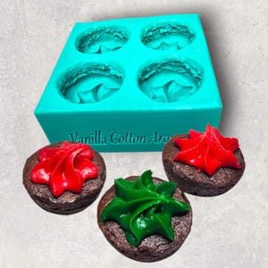 May include: A teal silicone mould with four circular cavities, and three frosted brownies. Two brownies have red icing, and one has green icing. The text "Vanilla Cotton Arts" is visible on the mould.