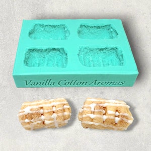 May include: A teal silicone mould with four rectangular cavities, labelled "Vanilla Cotton Aromas". Two finished cinnamon rolls with white icing are shown below the mould.