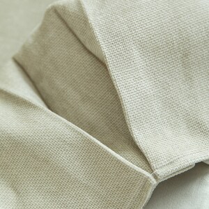 May include: Close-up of a beige fabric with a textured weave. The fabric is folded over itself, creating a seam.