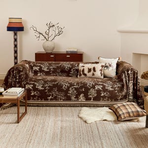 Könnte beinhalten: Ein braunes Sofa mit einer weißen und braunen gemusterten Wolldecke. Das Sofa hat zwei weiße und braune Kissen und einen weißen Teppich davor.