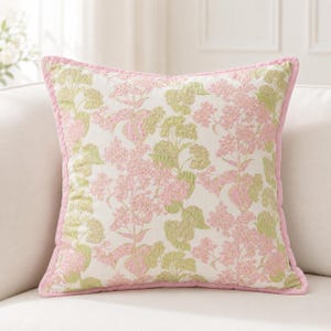May include: A square throw pillow featuring a cream-colored base with an embroidered floral pattern in shades of soft pink and light green. The pillow is finished with a solid pink piped edge that frames the entire square shape of the cushion.
