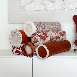 May include: A stack of five decorative throw pillows with different patterns and colours. The pillows are made of velvet and have a variety of textures. The pillows are arranged in a pyramid shape, with the largest pillow at the bottom and the smallest pillow at the top.